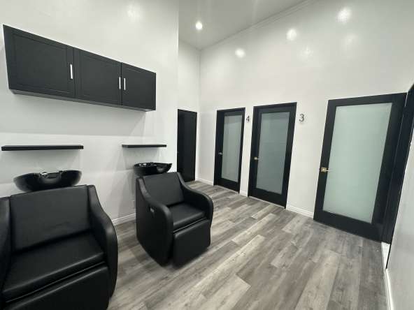 Modern salon hair wash stations with black chairs and sleek styling room doors.