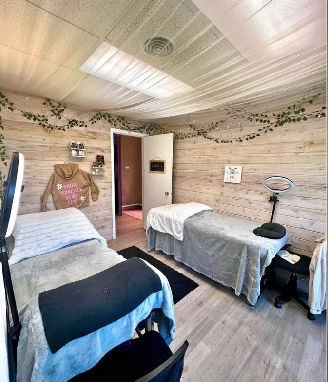 Bright salon treatment room with two massage beds, wood-paneled walls, and decorative greenery.