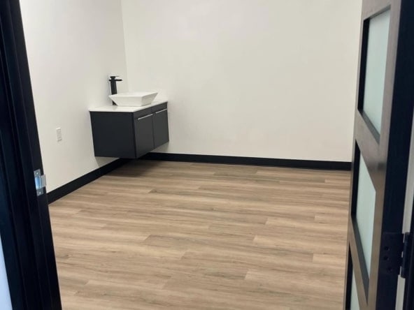 A clean, minimalist salon room featuring wooden floors, a sink, and a white wall, perfect for beauty business rental.