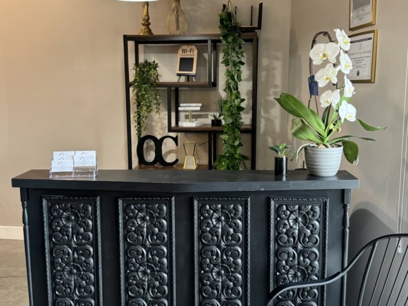 Stylish salon interior featuring a black reception desk, potted plants, and framed certificates.