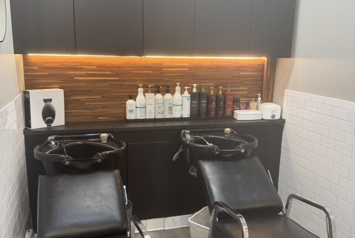 Hair washing station with shampoo bottles and styling chairs in a salon rental setting.