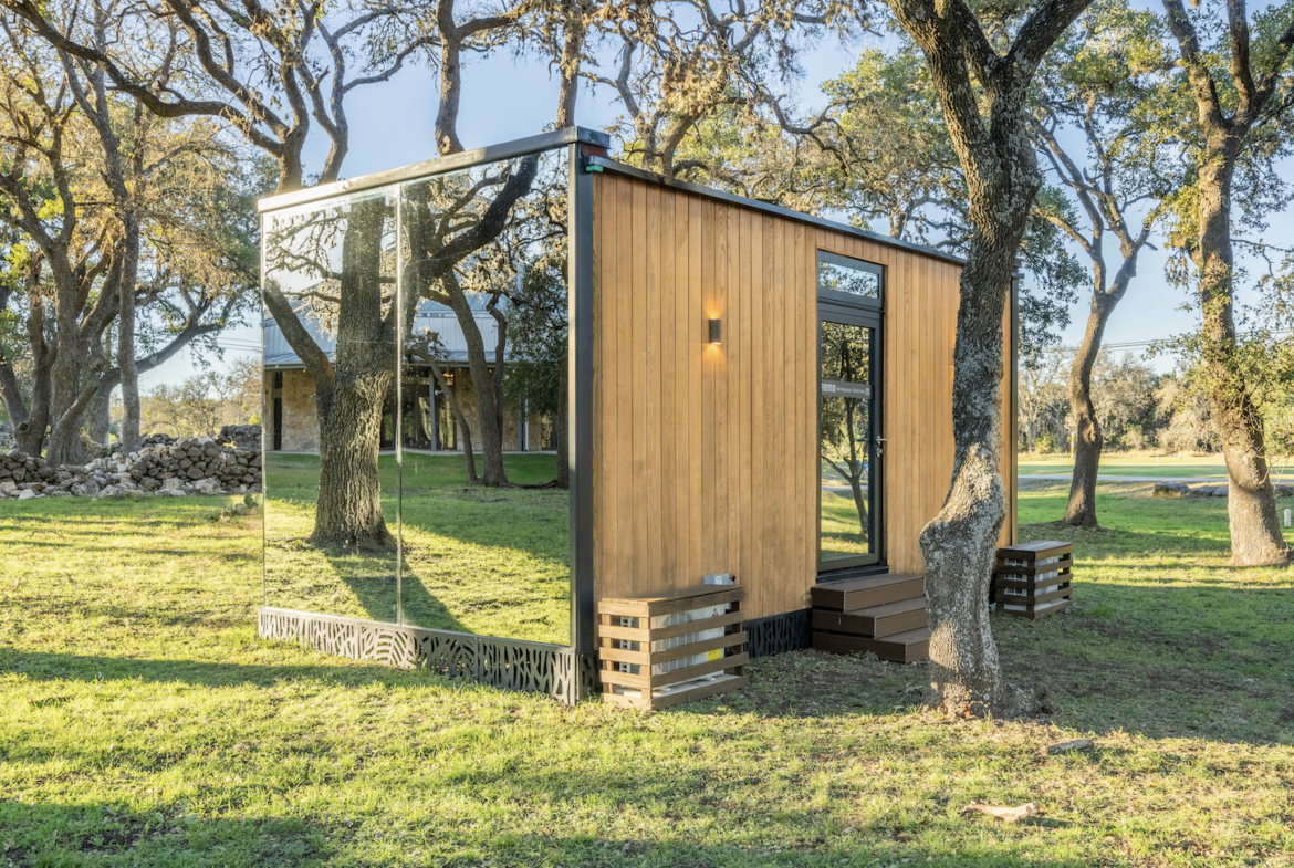 Eco-friendly tiny house with wood siding and large glass windows, surrounded by trees.