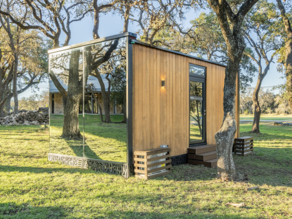 Eco-friendly tiny house with wood siding and large glass windows, surrounded by trees.