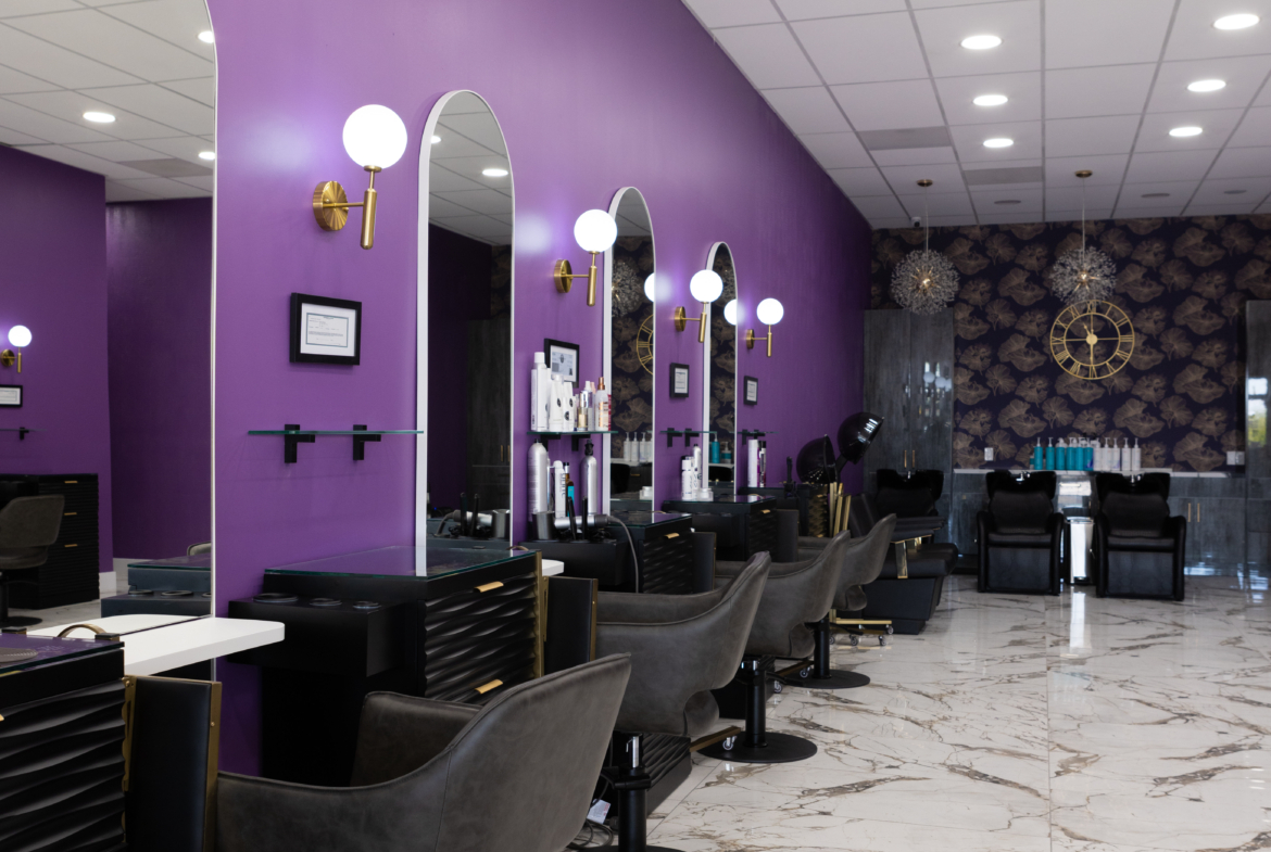 Stylish salon station with purple walls, mirrors, and black chairs for hair services.
