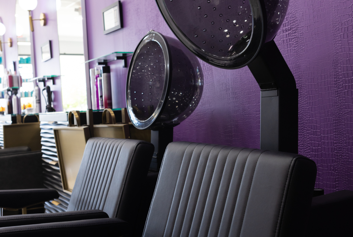 Stylish hair salon chairs with hair dryers against a vibrant purple wall in a modern salon.