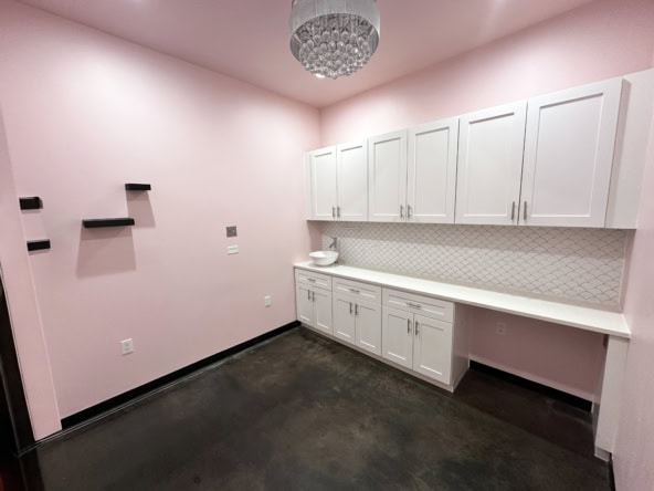 Modern hairstyling salon with white cabinets, pink walls, and workspace for beauty professionals.