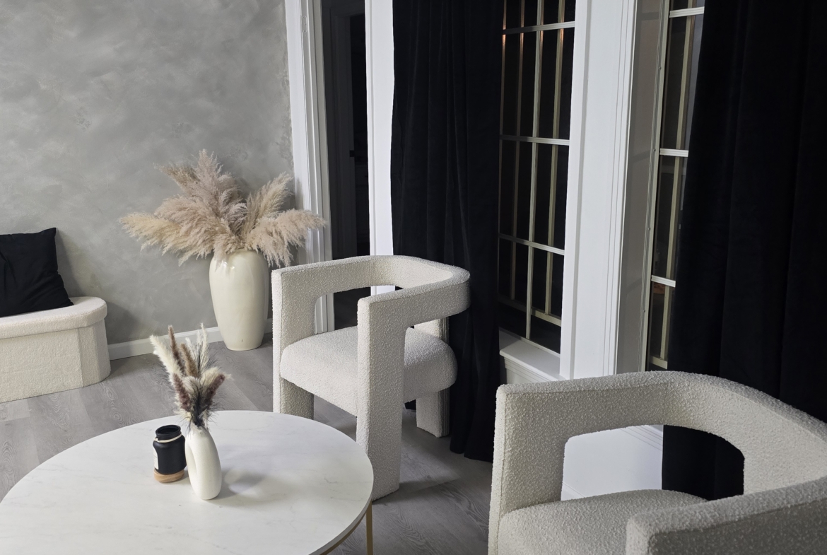Cozy salon lounge featuring white textured chairs, a marble table, and elegant curtains.