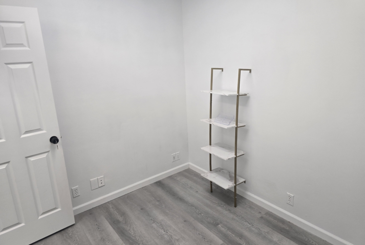 Spacious salon room with white walls, durable flooring, and versatile shelving for stylist use.