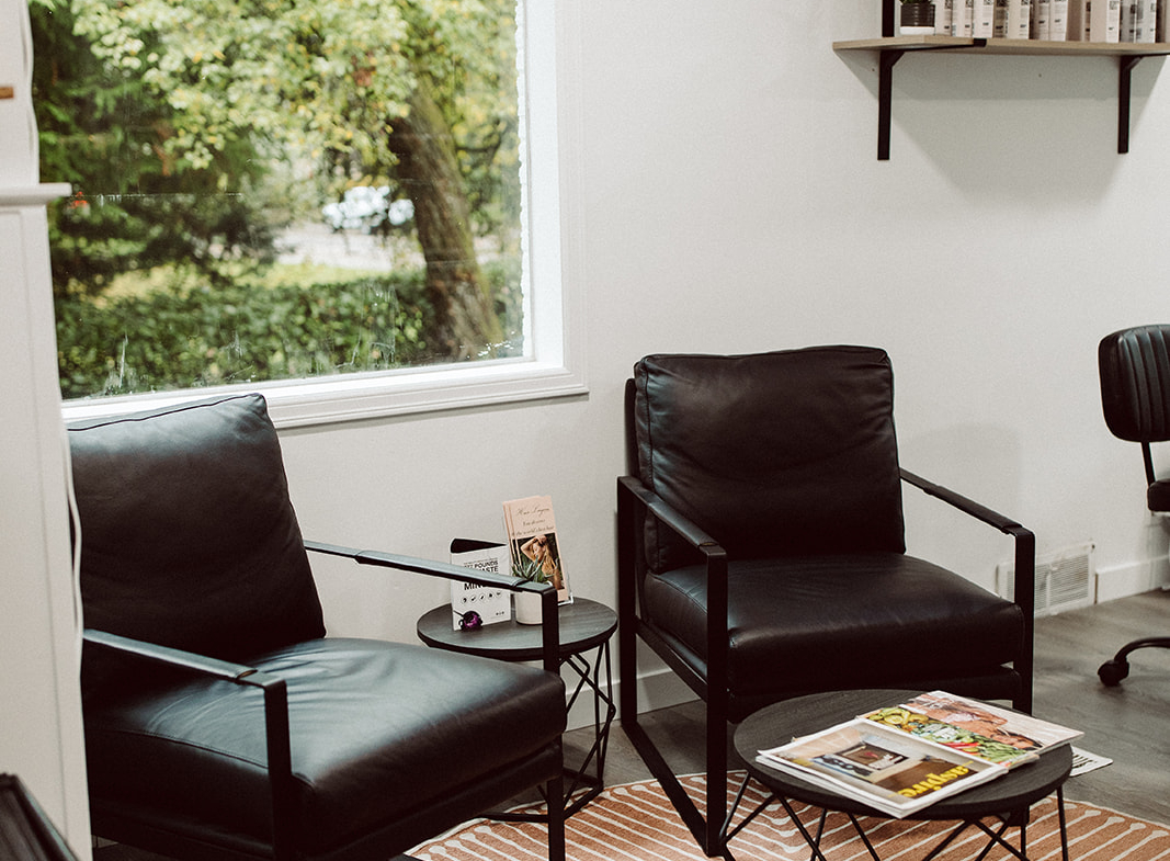 Modern salon waiting area with black chairs and large window overlooking greenery.
