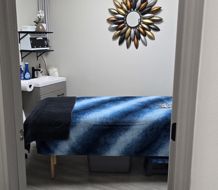 Relaxing massage therapy room with cozy treatment bed and decorative wall mirror.
