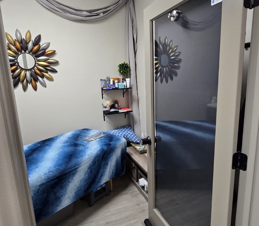 Well-lit salon space featuring comfortable bed, decorative wall mirror, and organized shelves.
