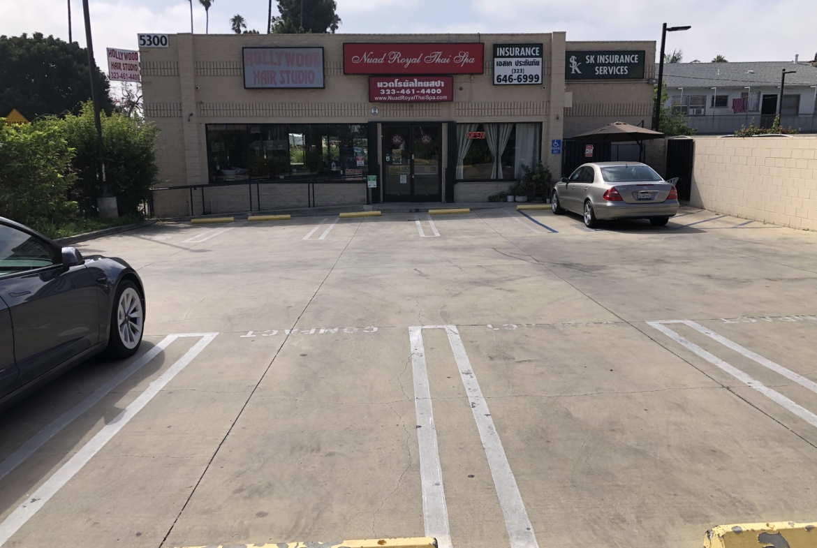 Empty parking lot in front of a hair salon and Thai spa, with designated spaces and clear signage.