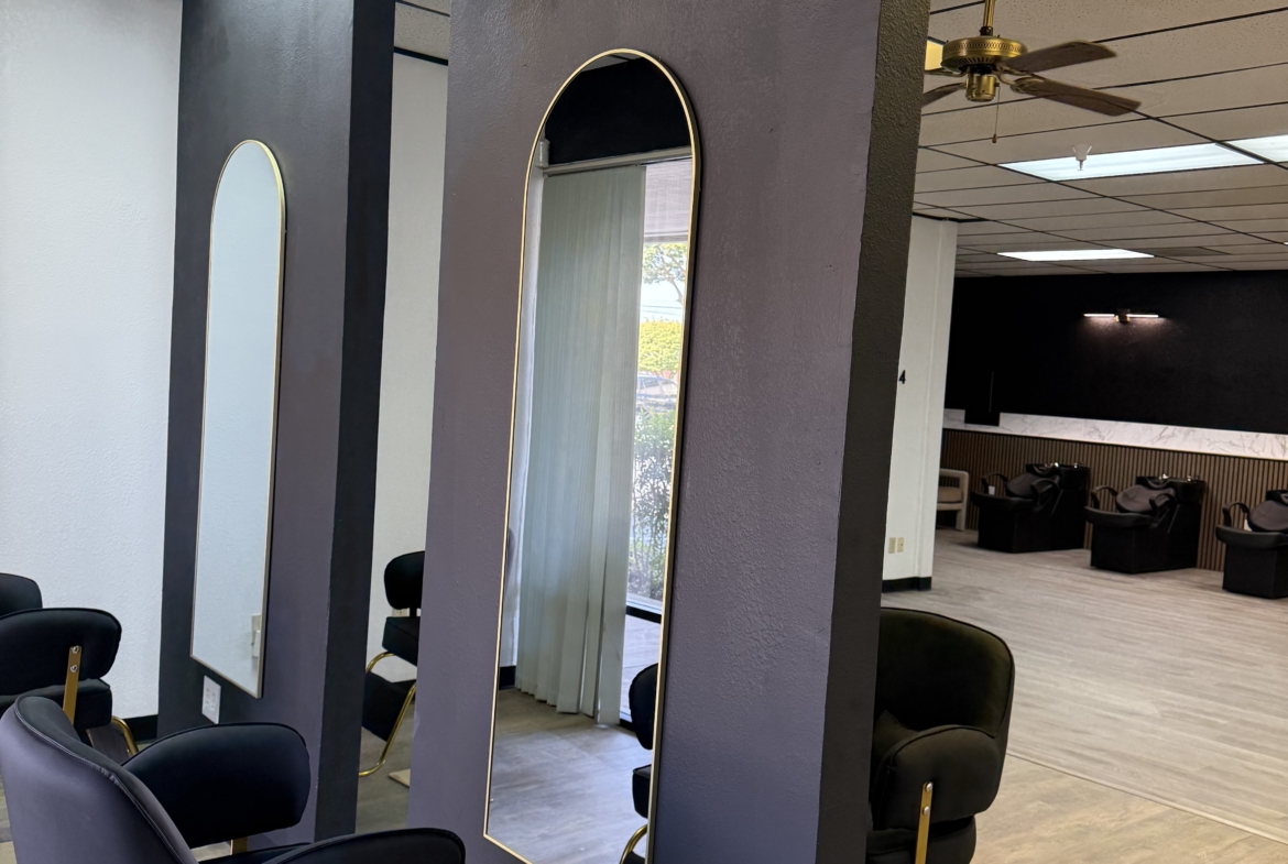 Elegant salon workspace with stylish mirrors, black chairs, and a spacious waiting area for clients.