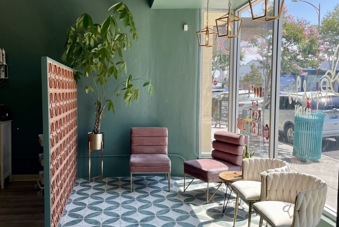 Cozy salon waiting room with pink and white chairs, green walls, and decorative lighting.