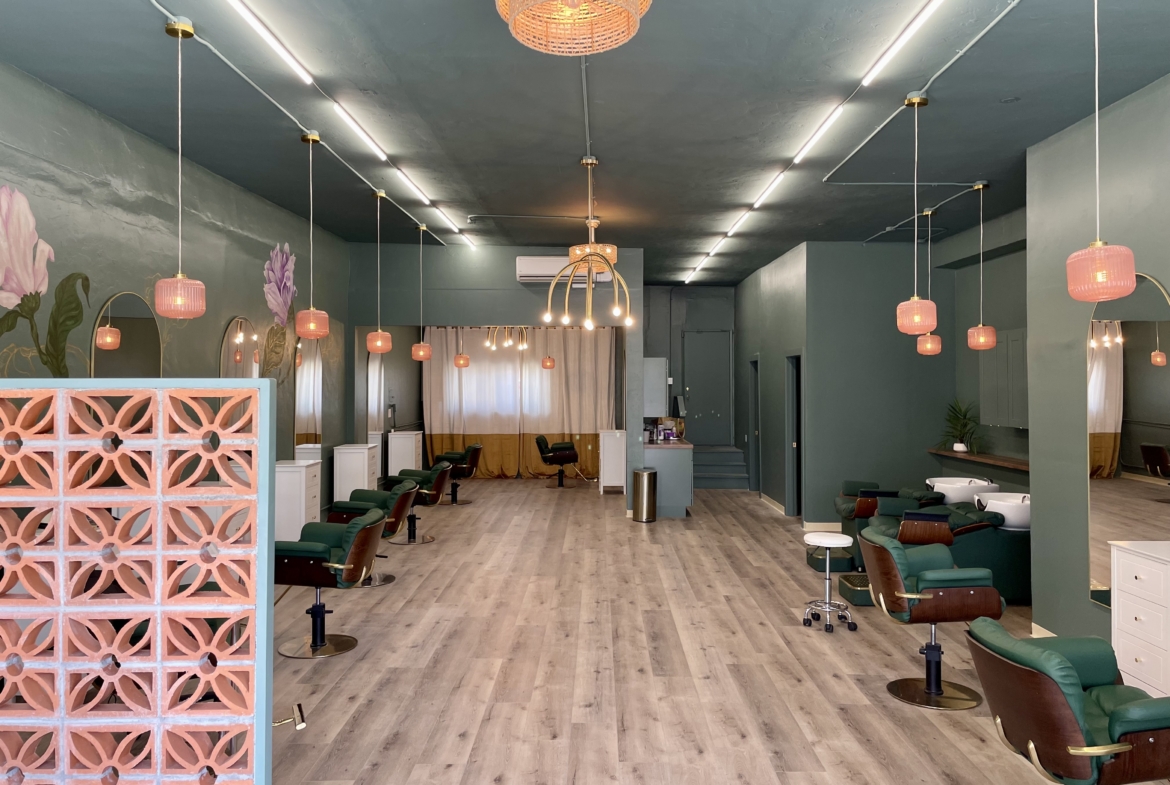 Spacious salon interior with green walls, stylish lighting, and multiple styling chairs for hair and beauty treatments.