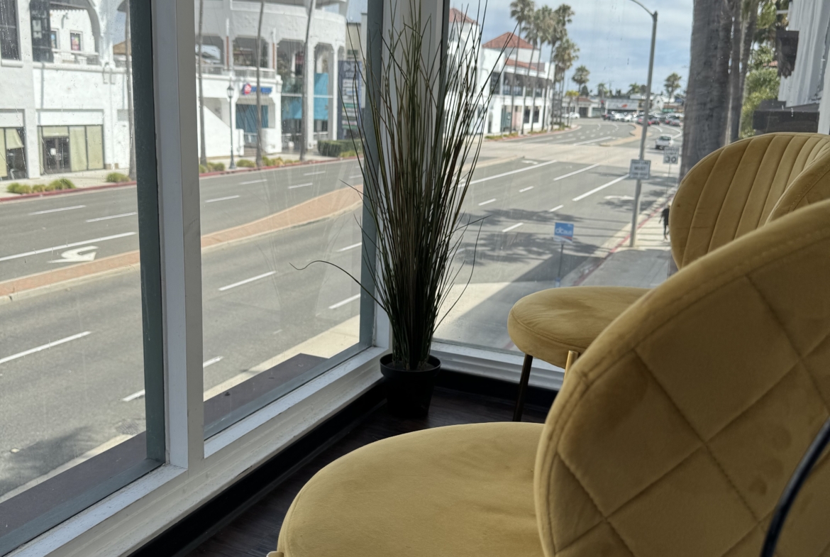 Bright salon waiting area with large window, cozy yellow chairs, and modern decor.