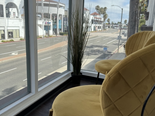 Bright salon waiting area with large window, cozy yellow chairs, and modern decor.