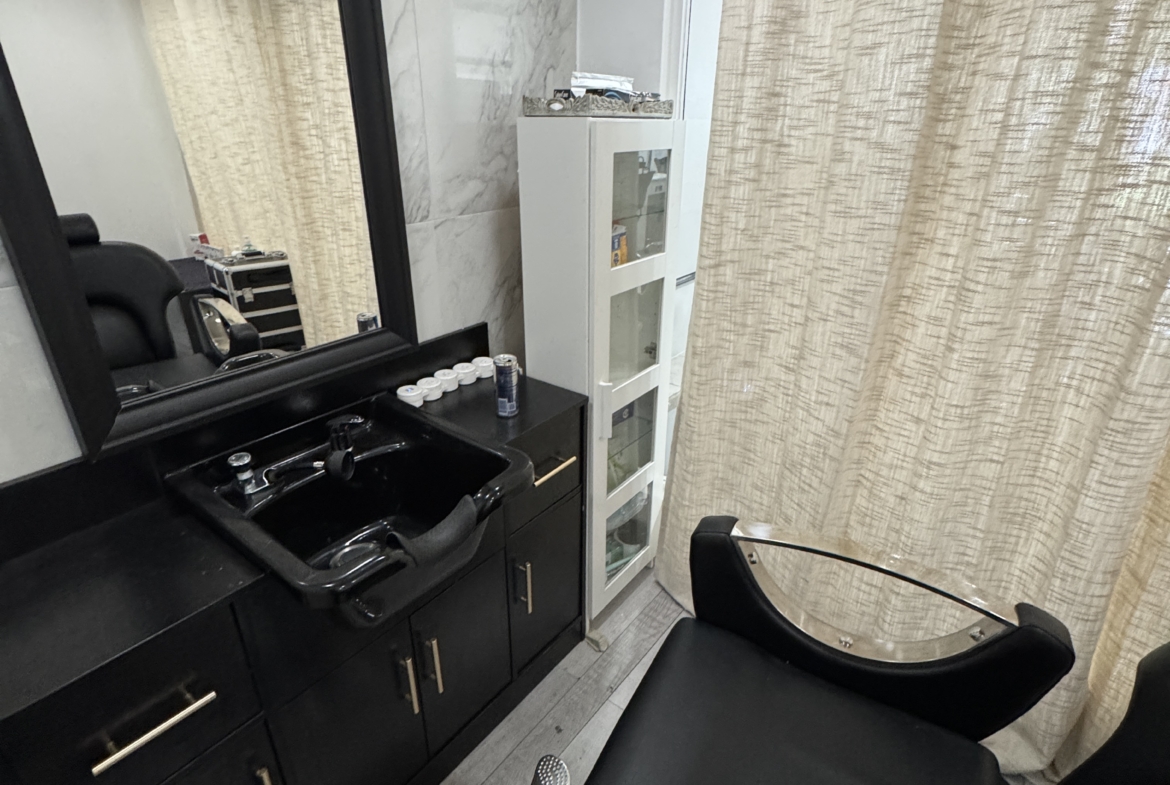 Salon shampoo and styling area with black furniture, mirror, and privacy curtains.