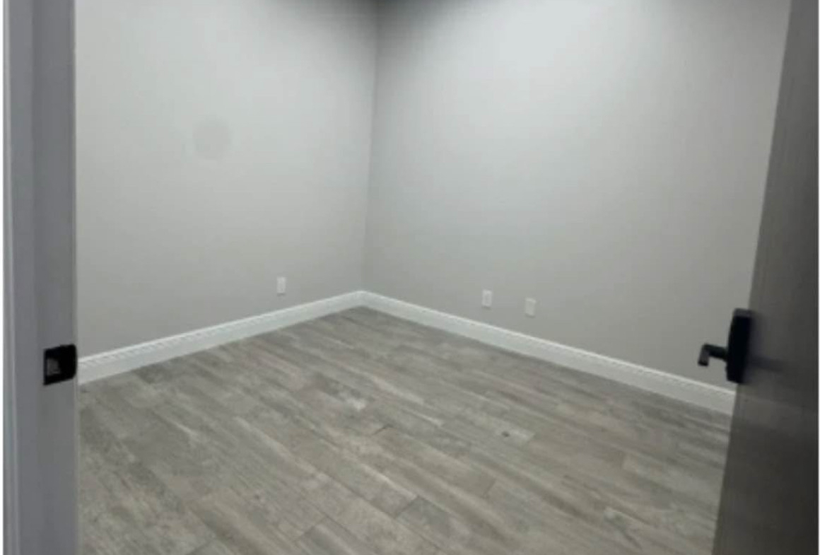 Bright, spacious salon rental room with neutral gray wooden floors and minimal decor.