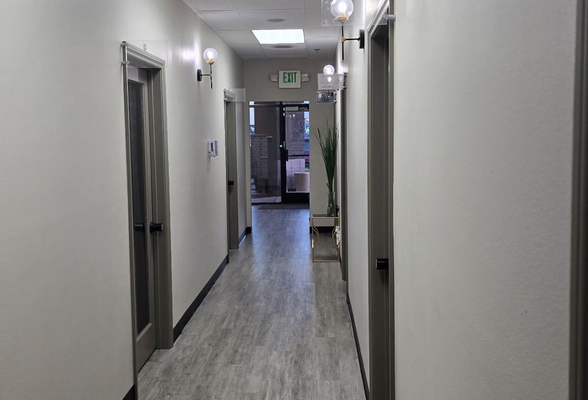 Hallway at Salon Renter featuring neutral walls, wood-look flooring, and stylish wall-mounted lighting.