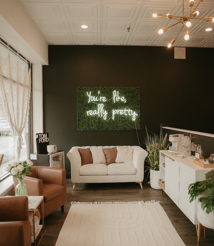 Stylish salon interior with comfortable seating, decorative plants, and inspiring neon message.