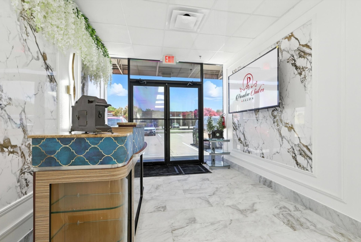 Elegant salon lobby featuring marble accents, floral decor, and a welcoming glass door entrance.