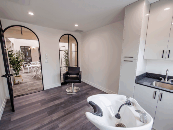 Clean, stylish salon room with styling chair, sink, and kitchen area for salon services.