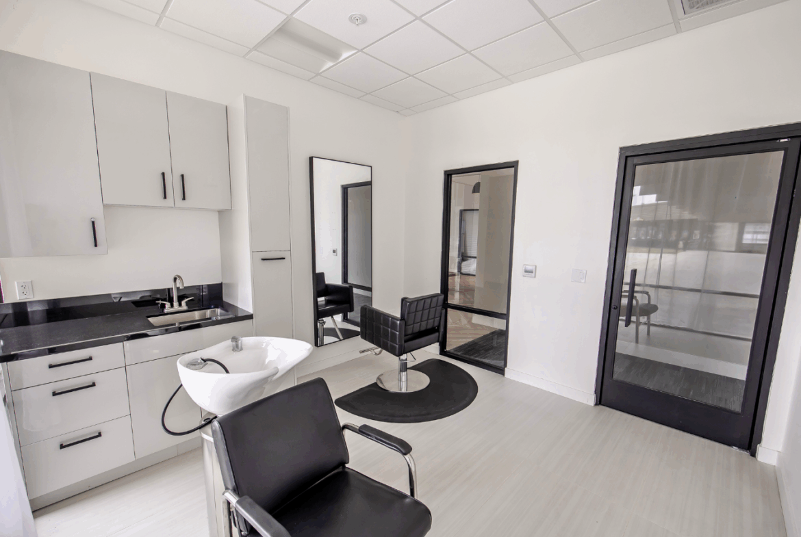 Bright salon space featuring white cabinetry, styling chairs, and a walk-in sink for hair treatments.