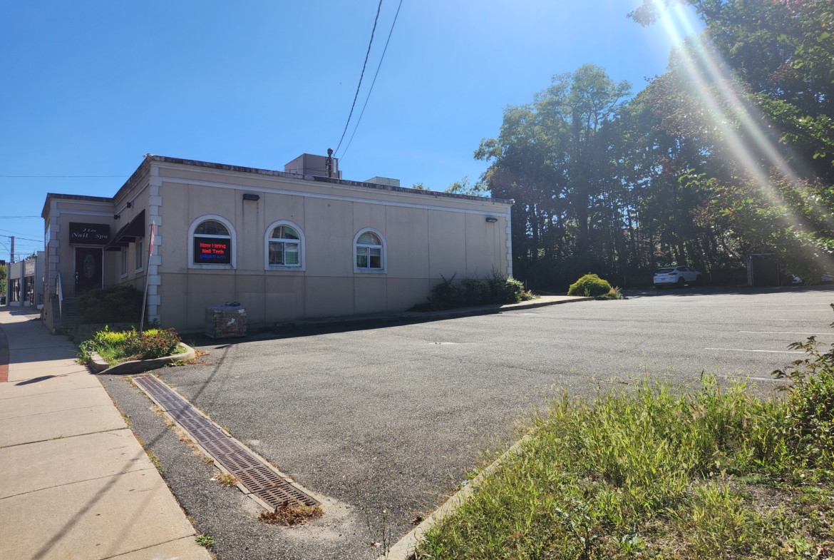 Bright daylight exterior view of a salon business with parking area and green surroundings.