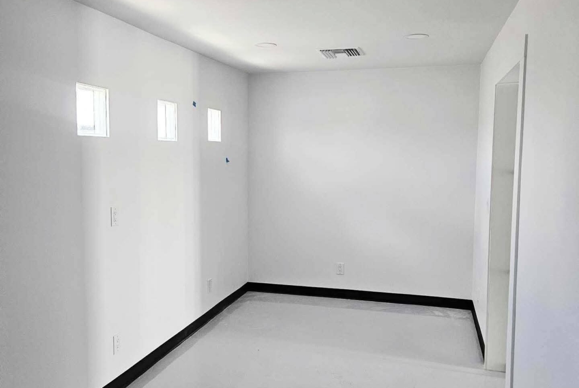 Empty salon rental with bright white interior, multiple small windows, and sleek black trim.