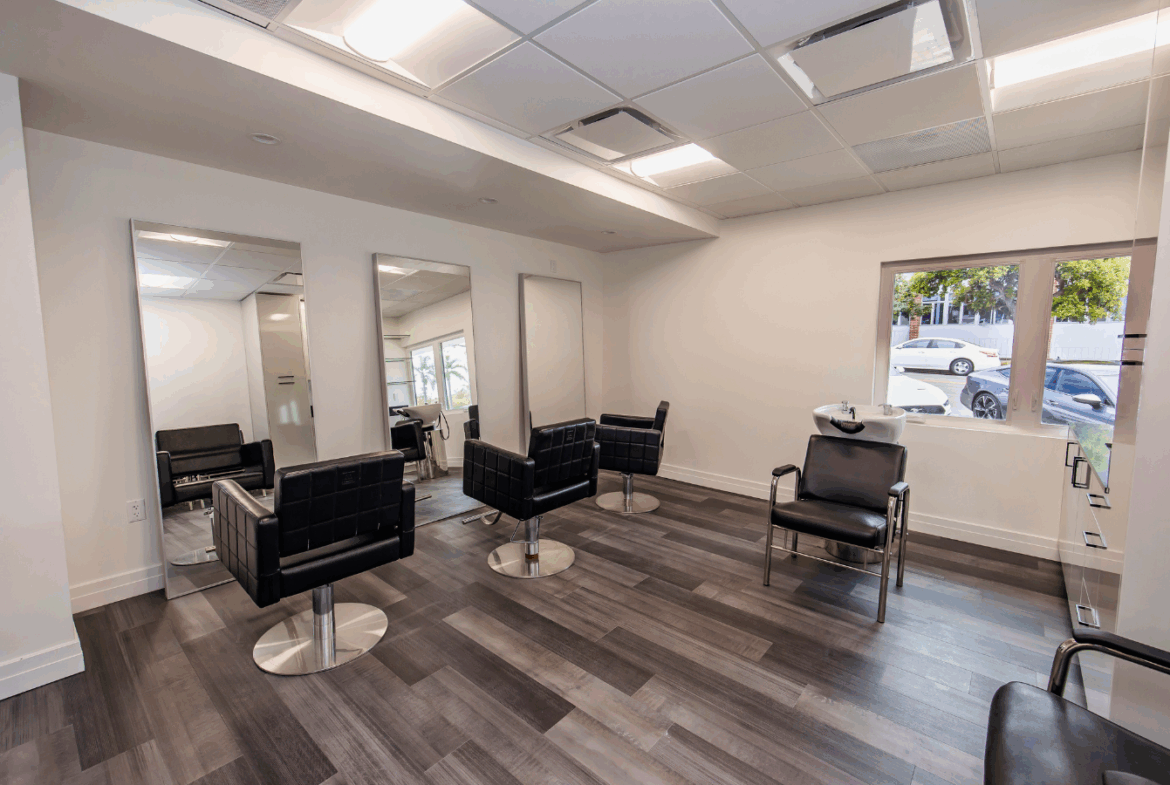 Bright salon with styling chairs, mirrors, and large window for rent or lease.