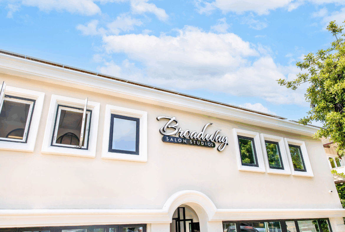 Bright exterior of a salon studio building with large windows and stylish signage, clear blue sky.