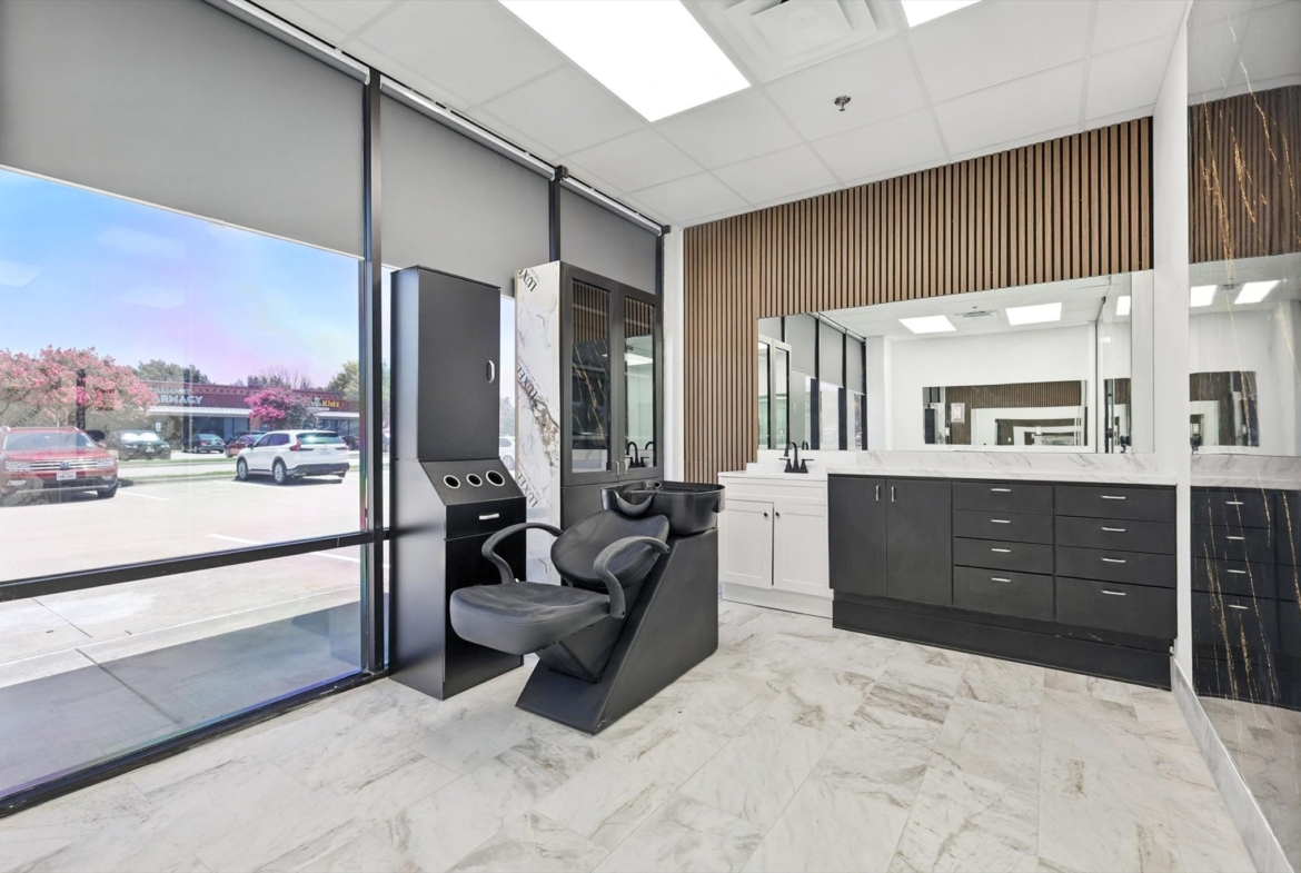 Bright salon space with styling chair, large windows, and organized countertops for rent.