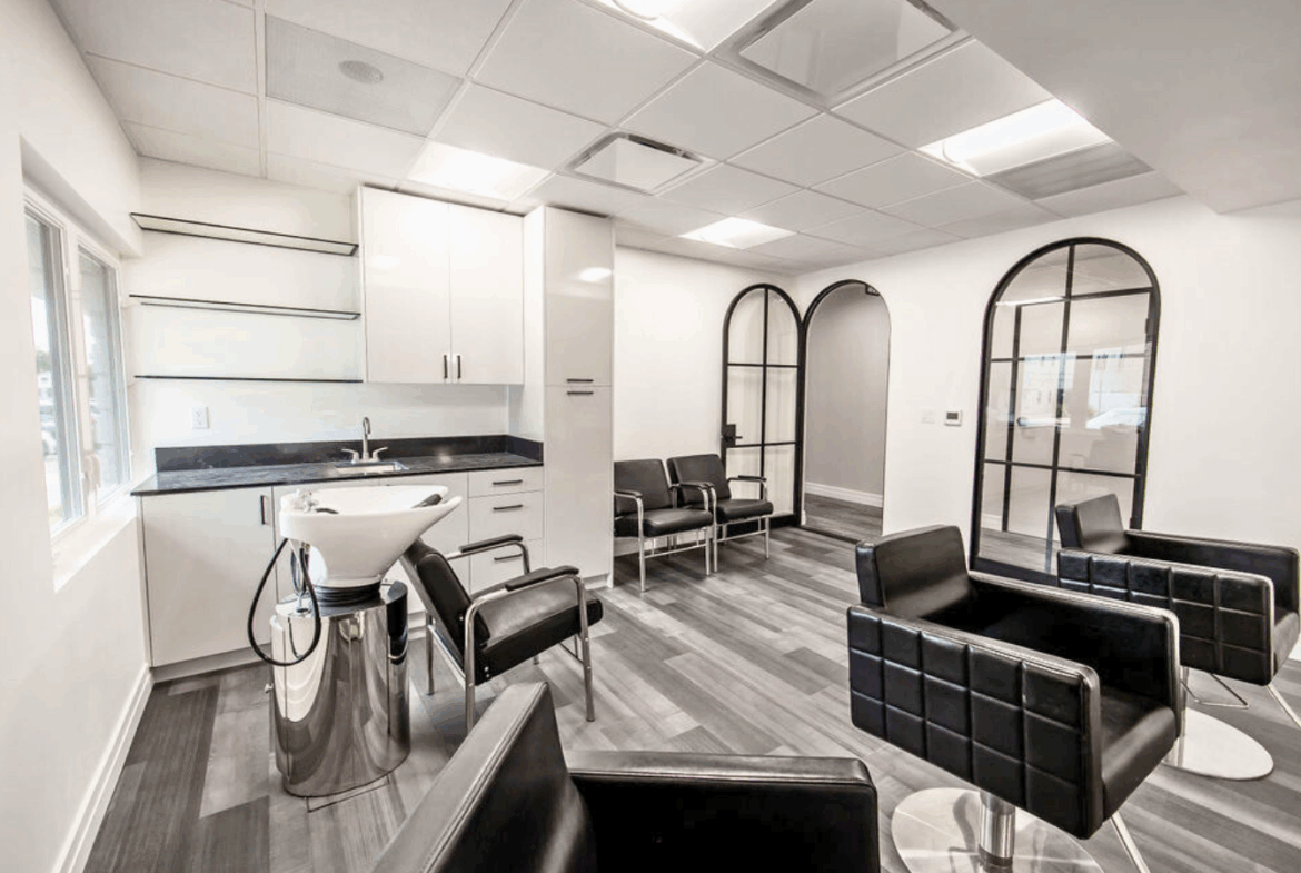 Bright, clean salon waiting area featuring black leather chairs, large windows, and stylish decor.