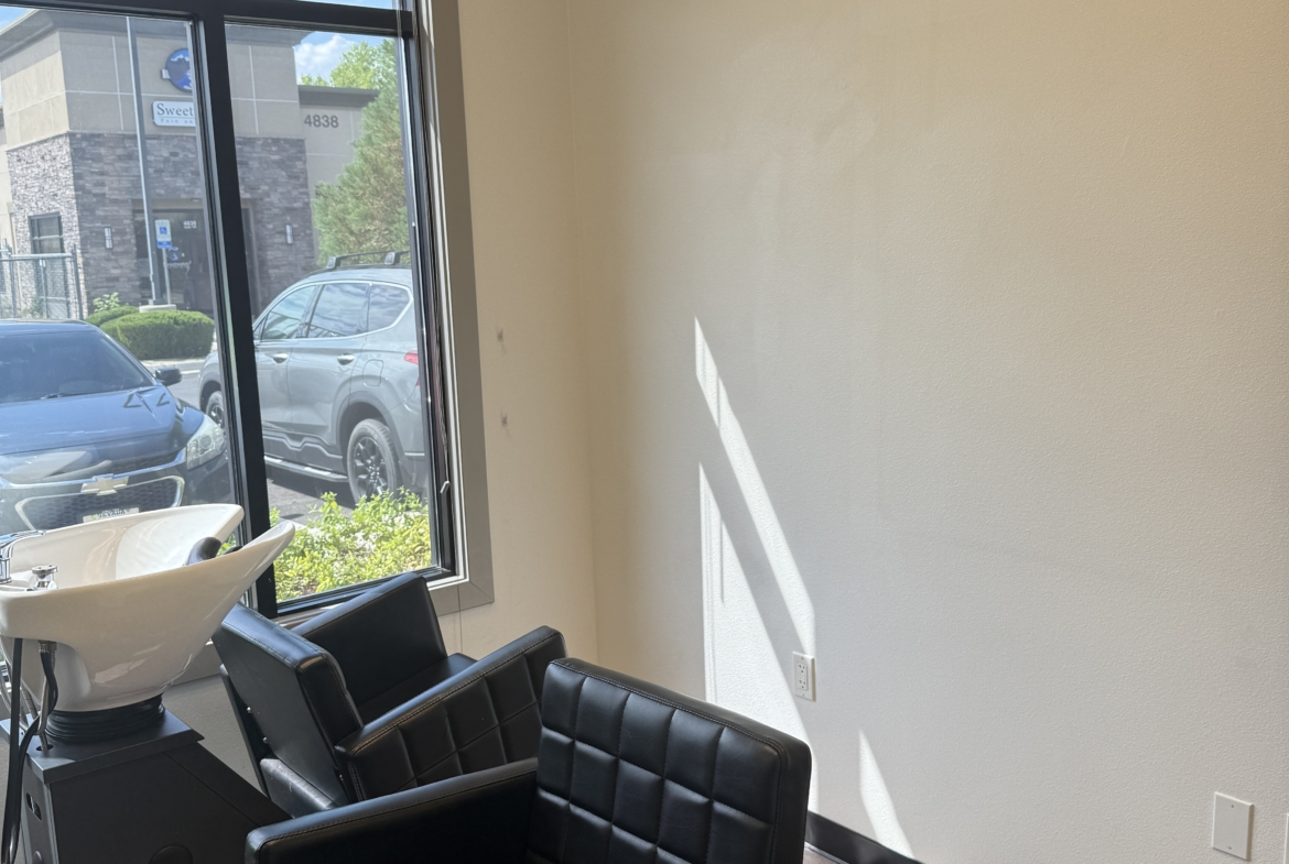Bright salon space featuring black styling chairs and a large window with natural light.