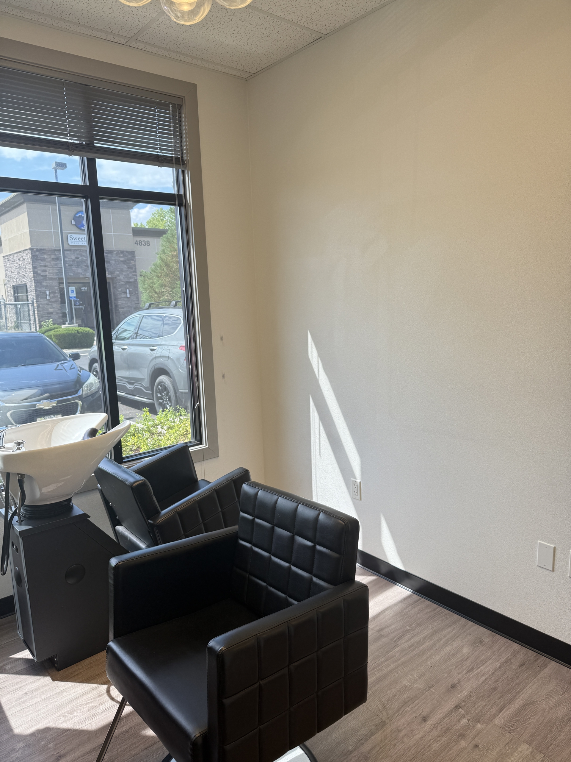 Bright salon space featuring black styling chairs and a large window with natural light.