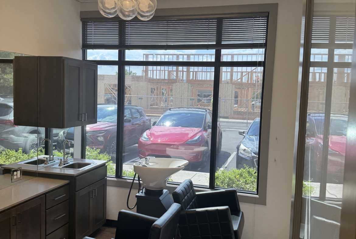 Salon interior with styling chairs, hair wash basin, large window, and contemporary lighting.