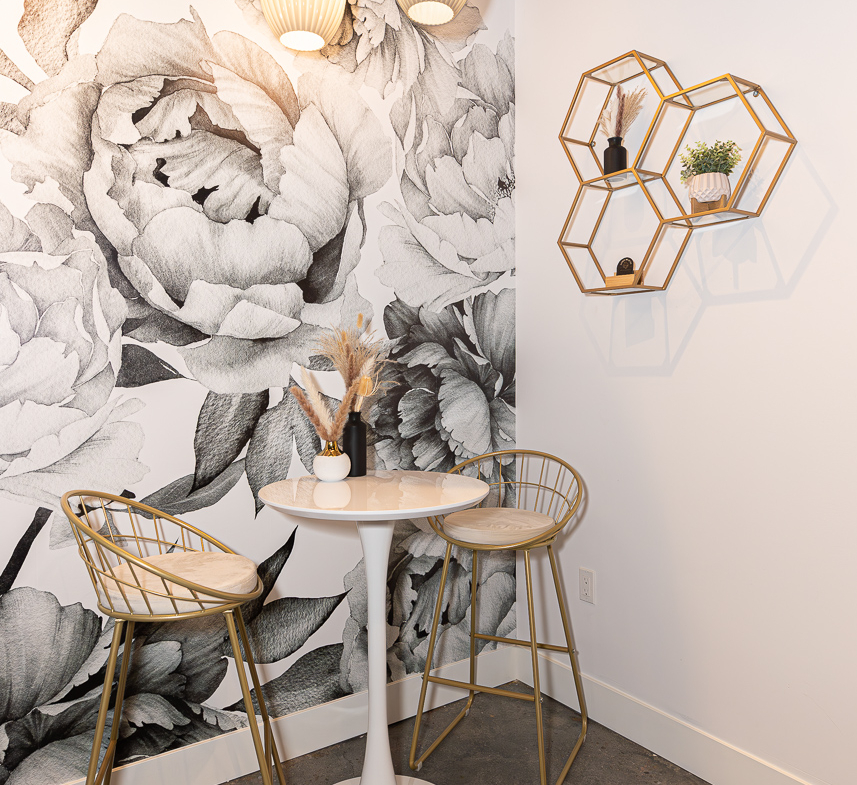 Modern salon seating with stylish gold chairs and floral wall decor.