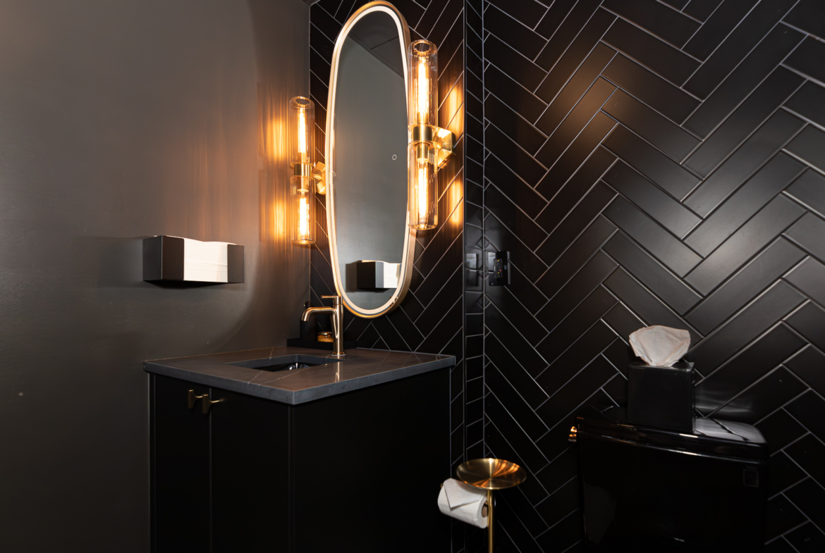 Elegant black-tiled bathroom with modern vanity, mirror, and warm lighting for salon use.