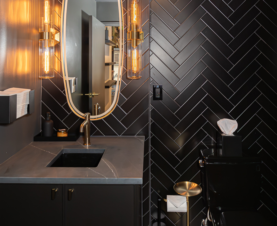 Elegant black herringbone wall tiles with modern lighting and fixtures.
