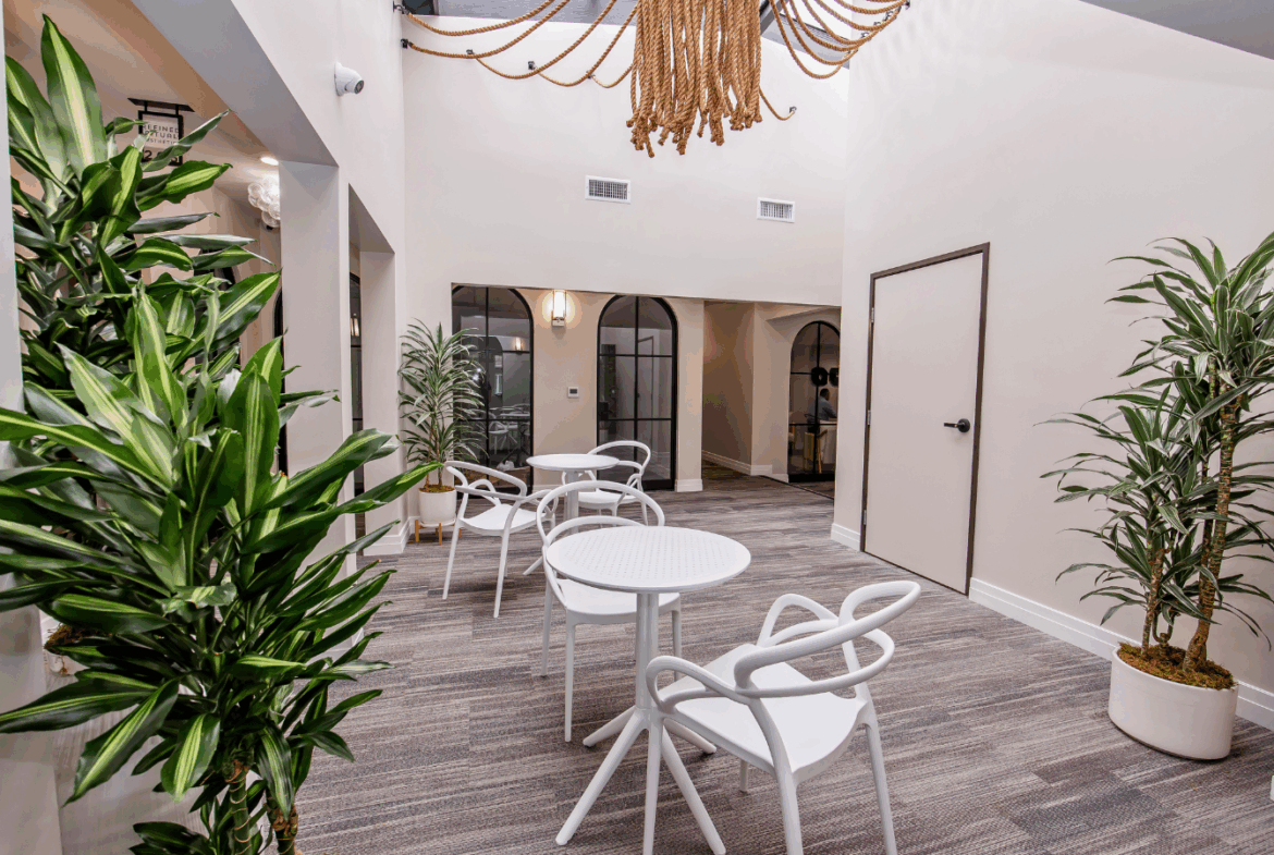 Modern salon interior with comfortable seating, white tables, and lush green plants.