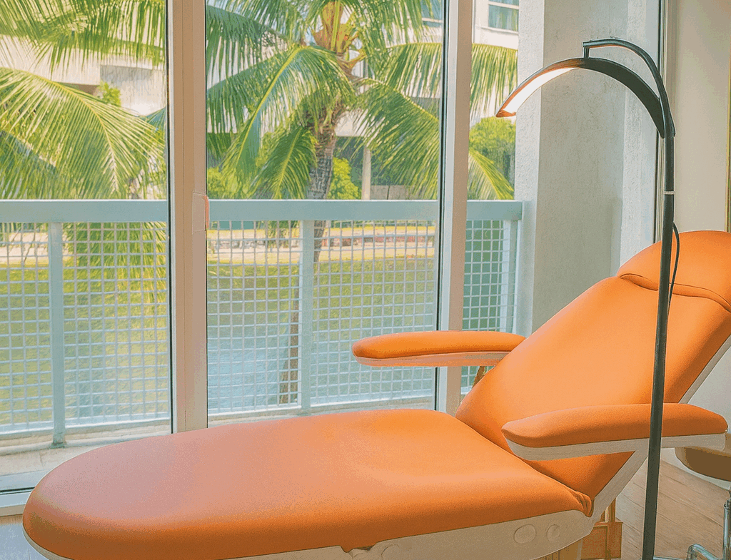 Bright, modern salon room with a comfortable treatment bed and natural light from large windows overlooking palm trees.