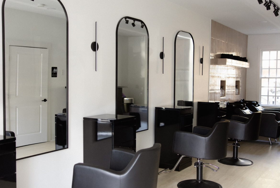 Modern salon interior with double mirrors, black chairs, and professional styling stations.