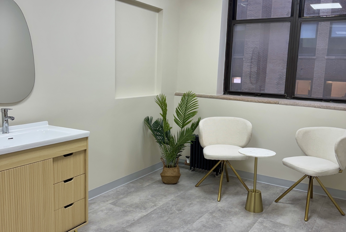 Bright salon waiting room with comfy chairs, potted plant, and large window.