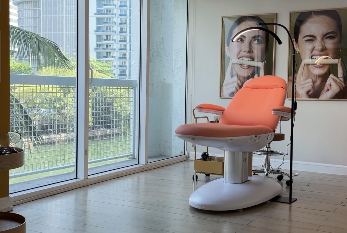 Bright beauty salon with modern treatment chair, large windows, colorful decor, and natural light.