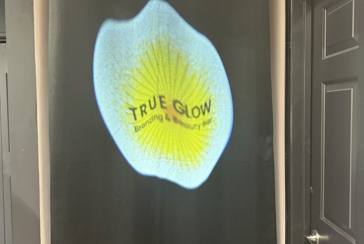 Projection of "True Glow" salon branding on black wall in beauty or hair salon.
