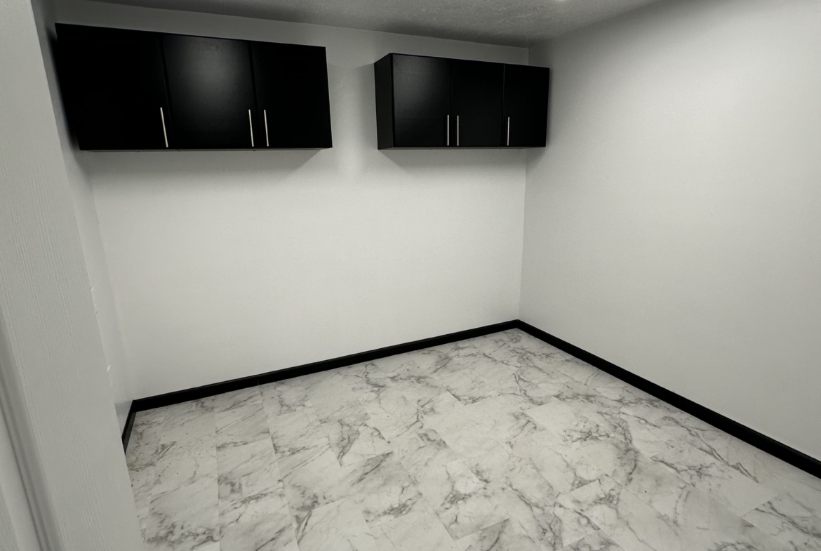 Empty salon storage room with white walls, black cabinets, and marble flooring.