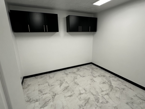 Empty salon storage room with white walls, black cabinets, and marble flooring.