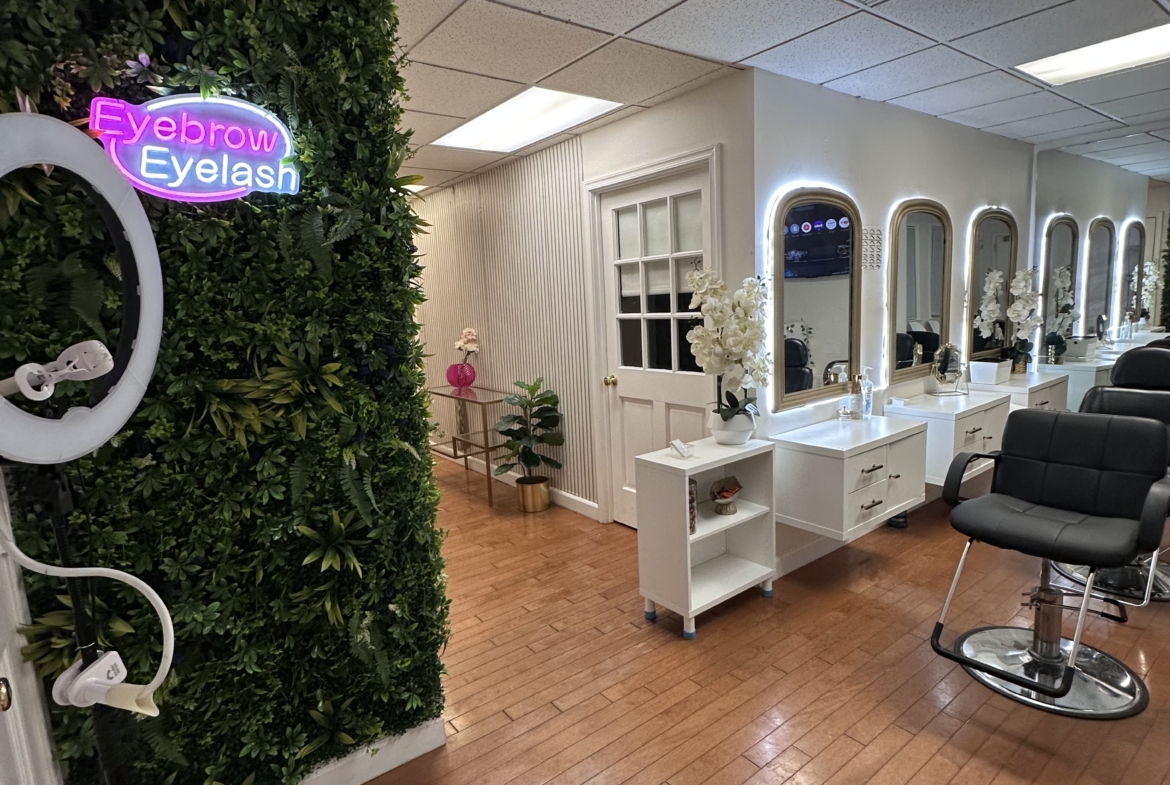 Neon "Eyebrow Eyelash" sign on a green wall decorates beauty salon focusing on eyelash and eyebrow services.