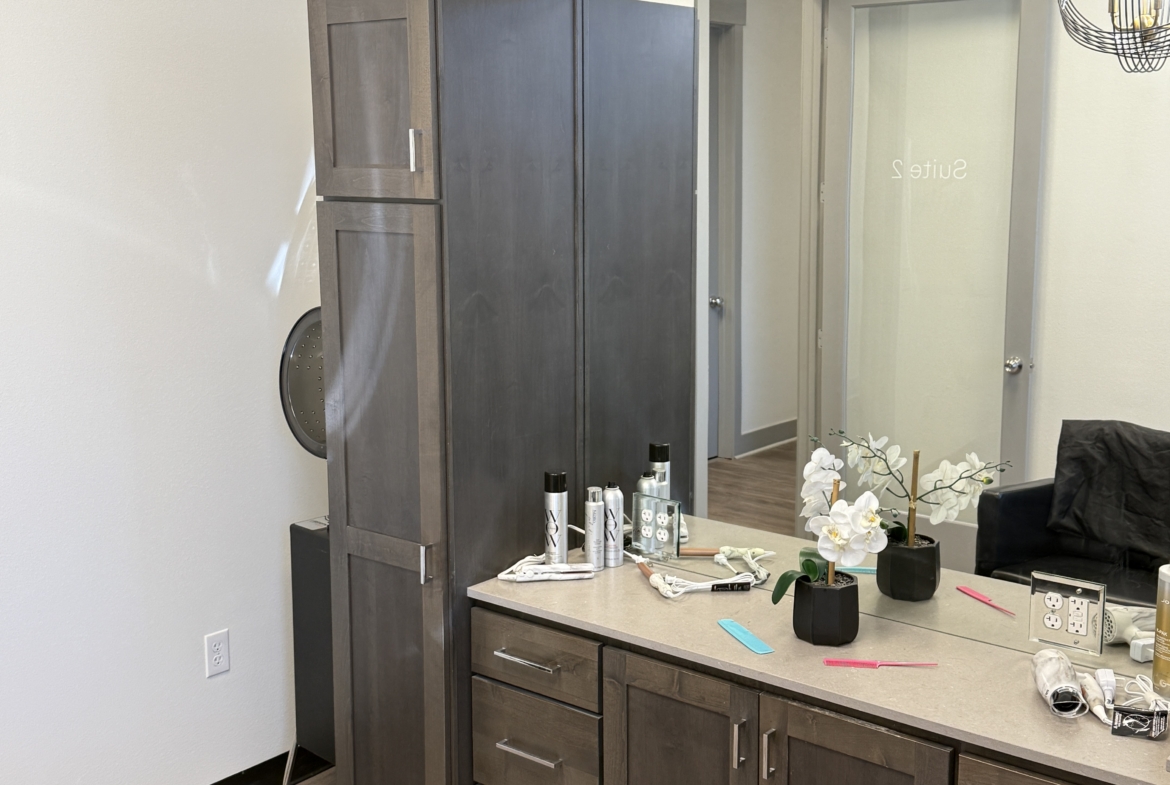 Modern salon rental workspace with a large mirror, wooden cabinets, and beauty products.